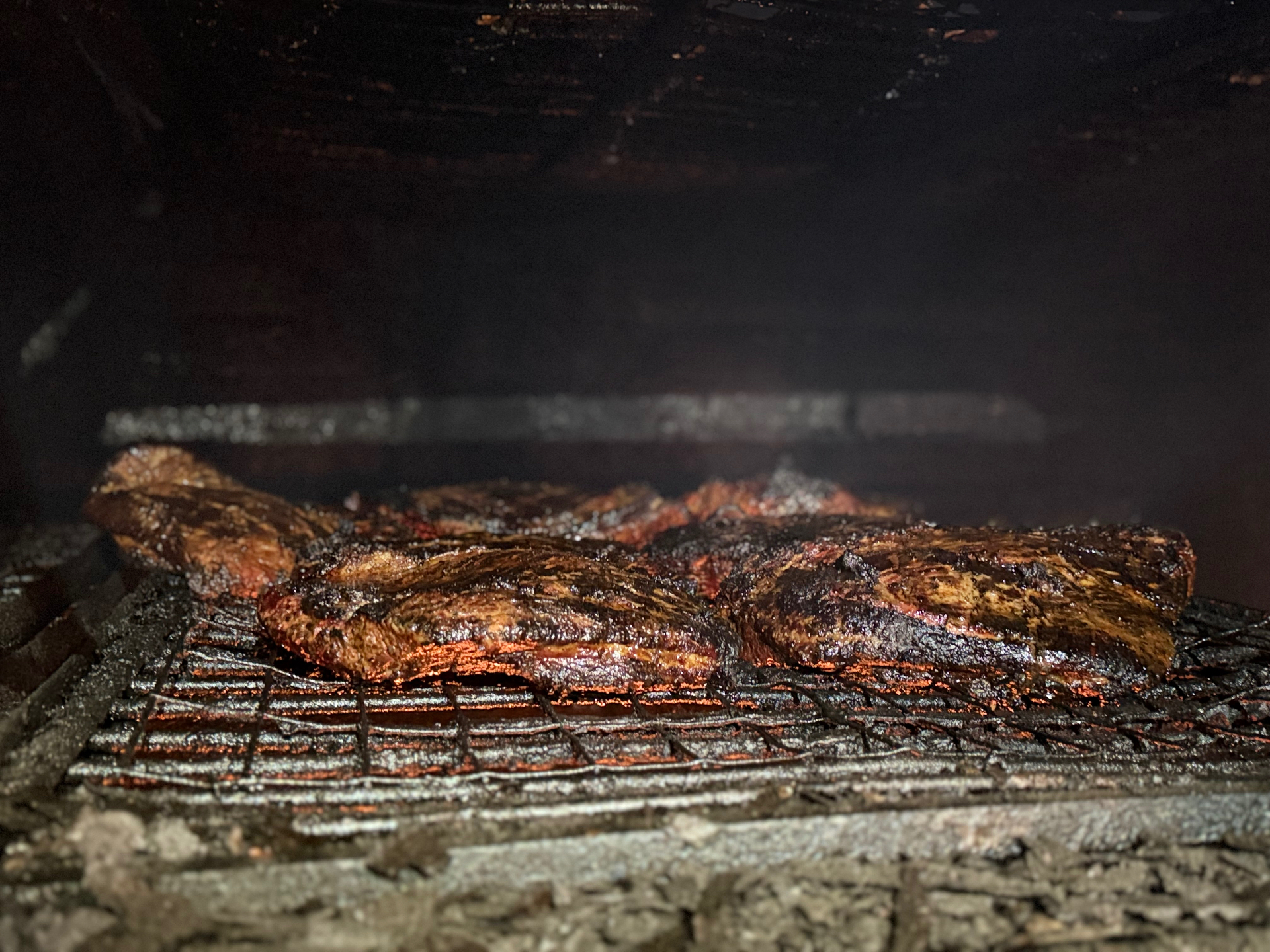 A row of briskets bark-side up over the embers in the Hilltop pit